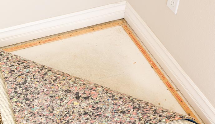 Partially pulled-back carpet revealing wooden tack strips along the edge of the floor