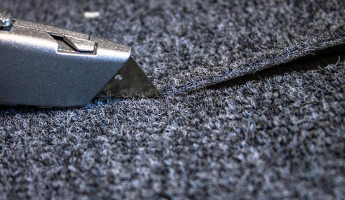 Precision cutting of dark gray textured carpet using a sharp utility knife