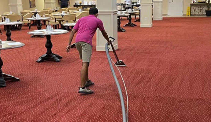 Professional cleaner using advanced equipment to clean a red carpet in a dining area