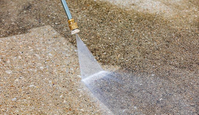 Professional using a pressure washer to remove grime from concrete