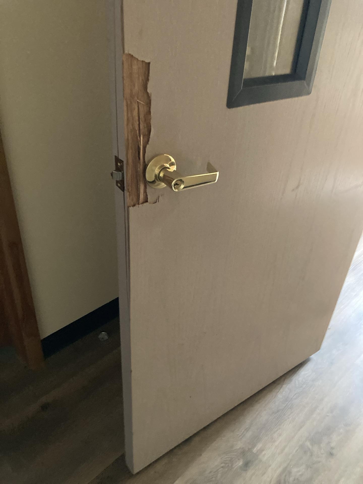 An interior church door with a split wooden frame and damaged lockset requiring professional repair.