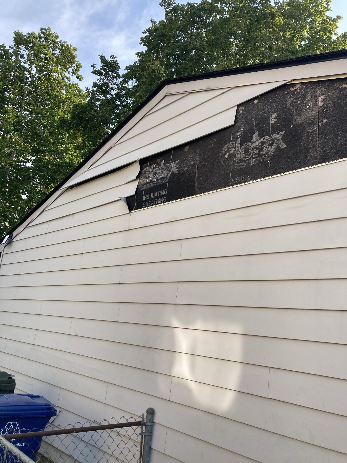Exposed insulating sheathing on a garage wall requiring professional vinyl siding put back installation.