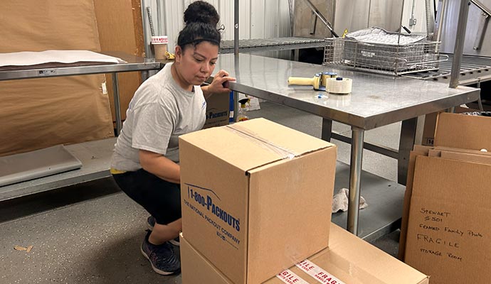 An expert carefully packing items into cardboard boxes in a storage or shipping area