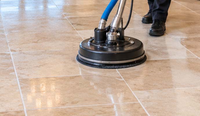 Person operating a floor scrubber on polished tile flooring.
