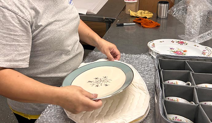 A professional carefully packing a floral plate with protective wrapping for moving or storage