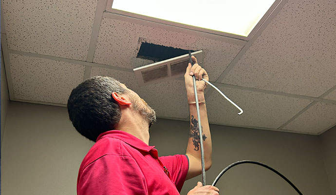 Technician cleaning ceiling air duct vent
