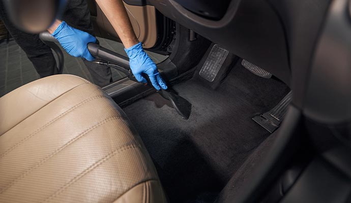Technician vacuuming car interior floor carpet