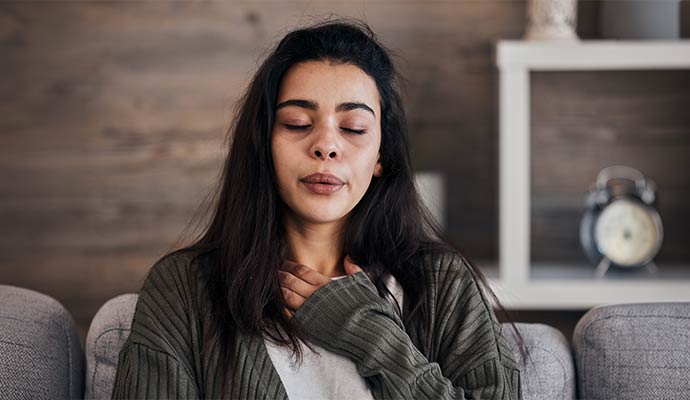 Woman sitting on a couch holding her chest and experiencing breathing discomfort