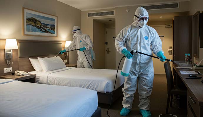 Workers in protective gear disinfecting a hotel guest room.
